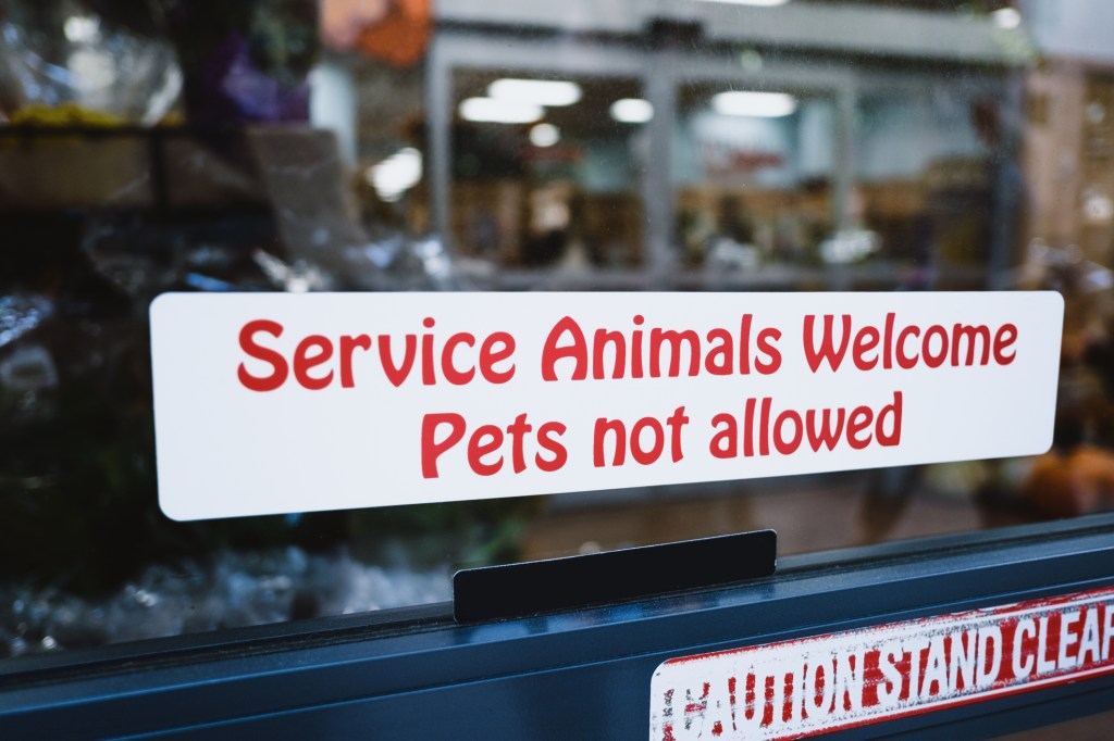 Primer plano de un cartel en el escaparate de una tienda de comestibles que indica que se admiten animales de servicio pero no mascotas.