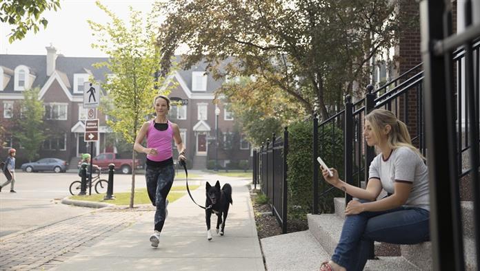 Női futó fut kutya és nő textil-val sejt telefon a szomszédos járdán