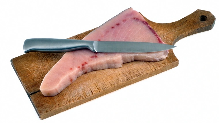Nyers kardhal steak egy vágódeszkán késsel, közelképben, fehér háttér előtt
