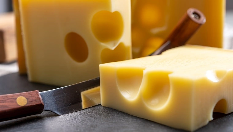 كتلة من الجبن الأصفر السويسري المتوسط ​​الصفر أو emmentaler مع ثقوب مستديرة وسكين الجبن عن قرب