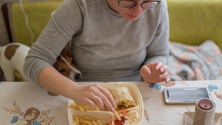 O tânără cu ochelari de vedere mănâncă fast-food la domiciliu