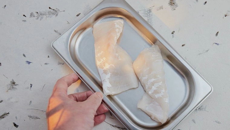 شرائح سمك القد في صينية مطبخ الفولاذ المقاوم للصدأ. سطح ديكور. تأثير الضوء العنبر.