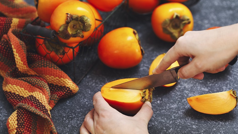 Manos de mujer cortando frutos frescos de caqui.