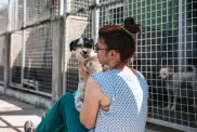 femeie care se întâlnește cu un câine mic din adăpost, amândoi stau în fața unor cuști